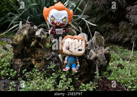 Figure Funko Pop tratte da film horror. Il clown malvagio Pennywise e la bambola del serial killer Chucky. Moody, cupo, spettrale, foresta verde scuro, ceppo di alberi. Foto Stock