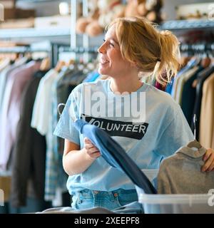 Lavoratrice di beneficenza femminile che seleziona le donazioni di abbigliamento al Thrift Store Foto Stock