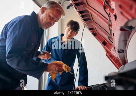 Meccanico auto maschio con apprendista che guarda sotto il cofano della vettura controllo del livello dell'olio con l'astina di livello Foto Stock