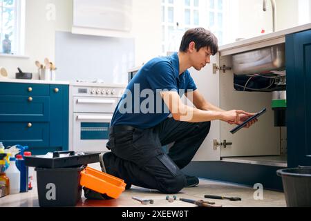 Idraulico maschio con unità di smaltimento rifiuti di fissaggio tablet digitale nel lavello da cucina domestico Foto Stock