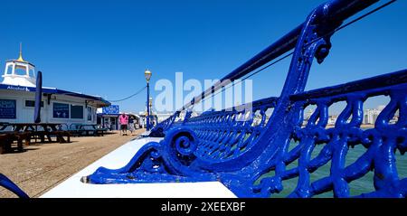 Una vista del Molo di Eastbourne mostra i posti a sedere in legno e una coppia che cammina lungo il Molo Foto Stock