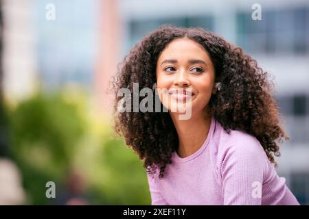 Primo piano donna che indossa un abbigliamento fitness seduto all'aperto e che trasmette in streaming agli auricolari wireless Foto Stock