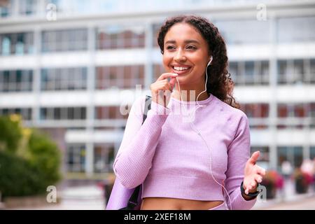 Donna che indossa abbigliamento fitness all'aperto che effettua una chiamata telefonica con microfono auricolare collegato al telefono cellulare Foto Stock