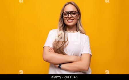 Donna bionda sorridente con scarsa vista che indossa occhiali su sfondo giallo Foto Stock