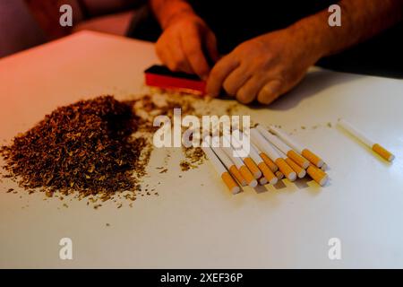 Mani maschili che tengono la macchina manuale per il tabacco da sigaretta, mucchio di shag tagliato fatto a casa per le sigarette, concetto di prodotti del tabacco costosi, cattivo Foto Stock