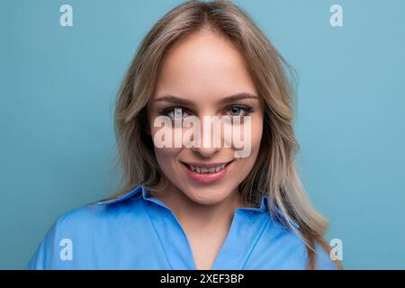 Ritratto di una giovane donna bionda adorabile che chiude graziosamente gli occhi su uno sfondo blu Foto Stock