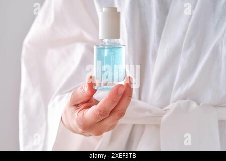 Siero blu con pipetta in mani femminili in un accappatoio. Foto Stock