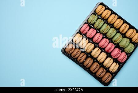 Macaron multicolore su sfondo blu in una scatola di plastica, vista dall'alto Foto Stock