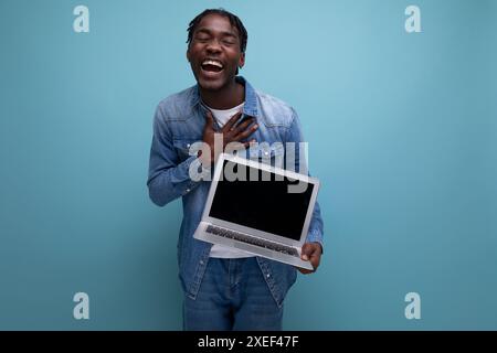 Un freelance di successo americano con dreadlock in giacca di denim lavora in remoto utilizzando un computer portatile Foto Stock