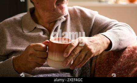 Primo piano di Man at Home in inverno salta con una bevanda calda calda calda di caffè in tazza Foto Stock
