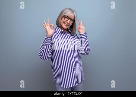 Elegante vecchia signora matura in una camicia alla moda su uno sfondo luminoso da studio con copyspace Foto Stock