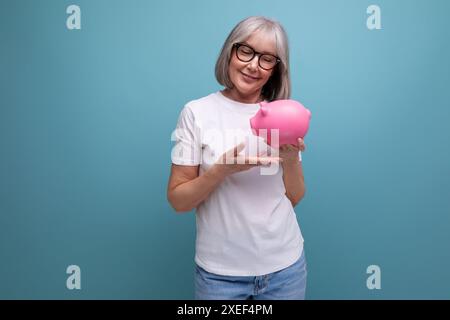 Una donna di anni maturi con i capelli grigi detiene il capitale di un salvadanaio su uno studio con spazio per le copie Foto Stock