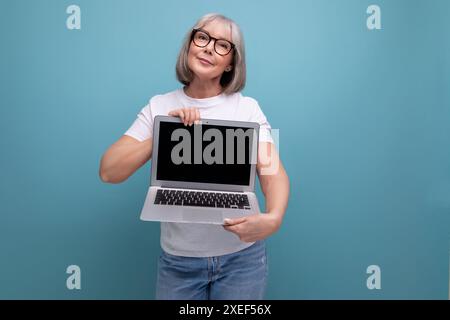 Affari di mezza età. donna di mezza età con capelli grigi che padroneggia la tecnica del laptop su sfondo studio con spazio per copie Foto Stock