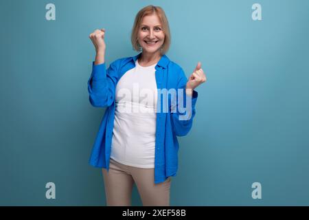 Ritratto di una donna bionda positiva anni '60 con elegante camicia blu su sfondo studio Foto Stock
