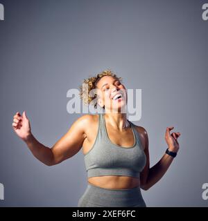 Foto in studio di una donna che indossa un abbigliamento fitness da palestra che danza nella classe Zumba su sfondo grigio Foto Stock