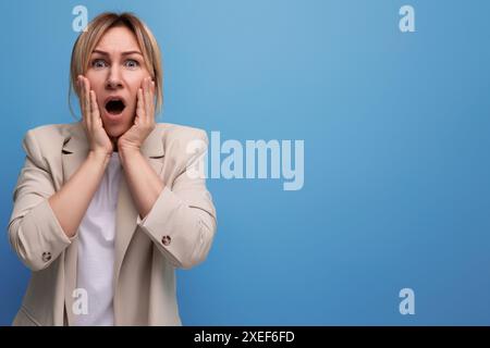 Indignata ha sorpreso la giovane donna europea in giacca a bocca aperta sullo sfondo dello studio Foto Stock