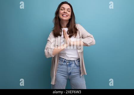 Gioiosa felice giovane signora dai capelli scuri in abiti informali che celebrano la vittoria su sfondo blu Foto Stock