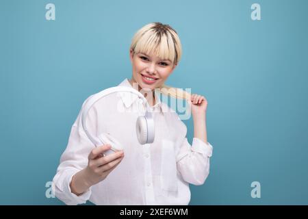 Una giovane donna bionda di successo che lavora in ufficio con camicia bianca e jeans usa le cuffie durante una pausa. concetto di business Foto Stock