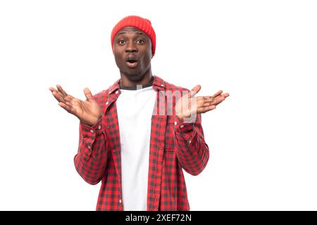 Sorpreso giovane africano positivo in cappello e camicia che raccontava notizie su sfondo bianco isolato Foto Stock