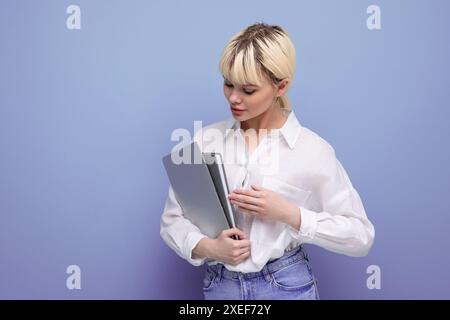 Giovane donna bionda di successo in camicia bianca e jeans con laptop e documenti Foto Stock