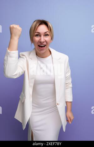 Giovane donna bionda, gioiosa e ben curata, con giacca e abito bianchi Foto Stock