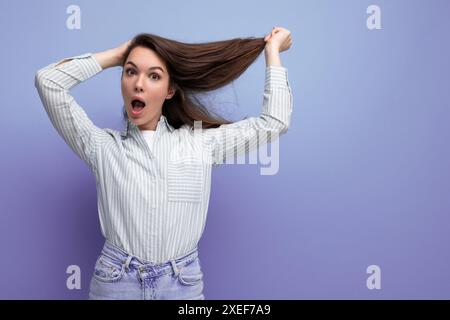 Affascinante giovane bruna adulta con eleganti capelli sani e setosi sotto le spalle in uno sfondo studio Foto Stock