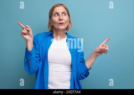 Sorpreso bionda donna matura nell'incredulità su sfondo blu con copyspace Foto Stock