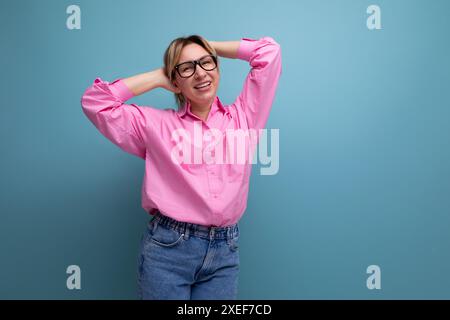 Modello donna caucasica giovane e positivo con capelli a coda di cavallo dal look elegante composto da camicetta rosa e jeans Foto Stock