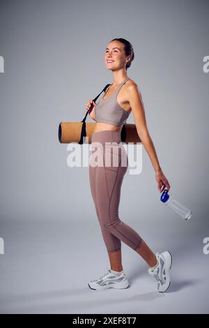 Studio Portrait of Woman in Gym fitness Clothing with Gym Mat e Holding Water Bottle Foto Stock