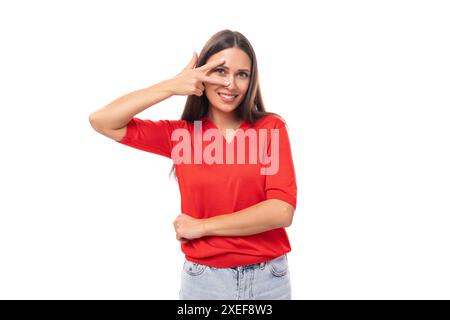 La giovane e affascinante signora bruna vestita con una t-shirt rossa sorride dolcemente su uno sfondo bianco Foto Stock