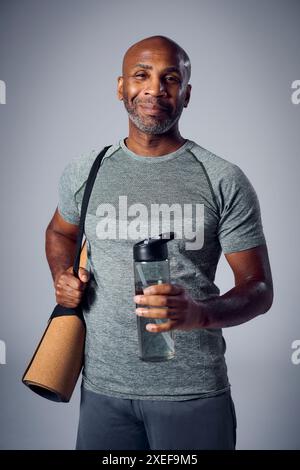 Studio Ritratto di uomo maturo sorridente in palestra abbigliamento fitness con tappetino per esercizi e bottiglia d'acqua Foto Stock