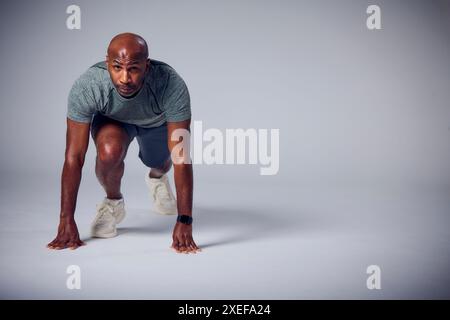 Primo piano in studio dell'uomo maturo con l'abbigliamento fitness da palestra che inizia la corsa Sprint su sfondo grigio Foto Stock