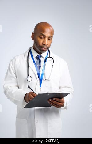 Studio Ritratto del medico maturo che indossa un cappotto bianco scrittura sulla cartella paziente sulla clipboard Foto Stock