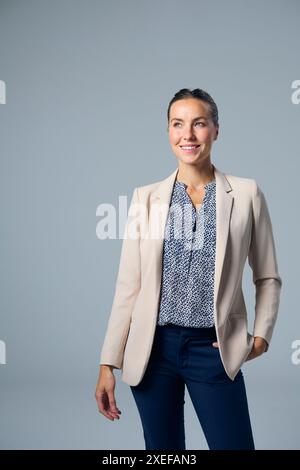 Studio Ritratto di una donna d'affari sorridente che indossa un abito con la mano sull'anca su sfondo grigio Foto Stock