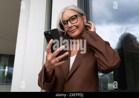 Bella donna d'affari matura di successo dai capelli grigi ama controllare i messaggi sullo smartphone Foto Stock