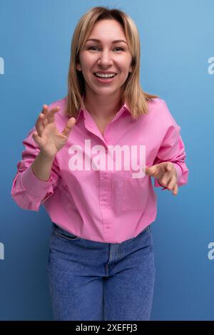 Giovane donna bionda operaia europea con capelli fluenti in una camicetta rosa sorride dolcemente Foto Stock