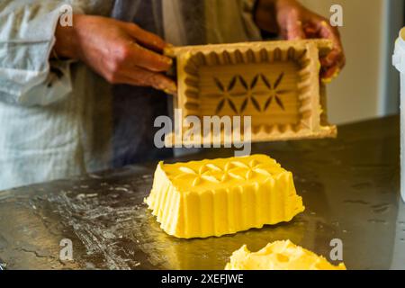 Produzione di burro nel caseificio appartenente al Filzmoosalm. Il burro alpino giallo dorato viene porzionato utilizzando una tradizionale muffa di legno. Promegg, Großarl, Salisburgo, Austria Foto Stock