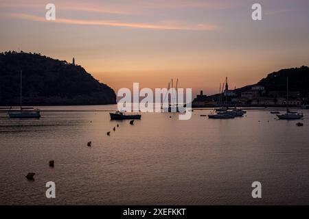 Vista all'ingresso del porto di Port de Sóller con barche a vela ancorate sulle acque tranquille sotto il bagliore del sole che tramonta, ideale per mostrare Maiorca Foto Stock