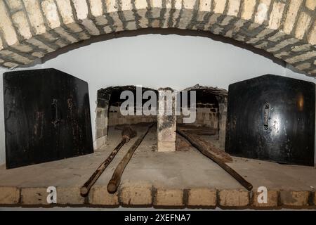 Due tradizionali forni in mattoni a legna con porte di ferro aperte e utensili con manico lungo appoggiati sul focolare dei mattoni Foto Stock