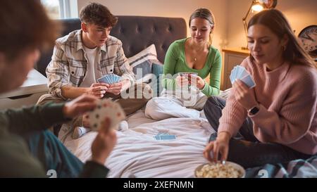 Un gruppo di adolescenti e ragazzi a casa che si divertono ridendo e giocano a carte in camera da letto insieme Foto Stock