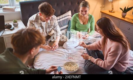 Un gruppo di adolescenti e ragazzi a casa che si divertono ridendo e giocano a carte in camera da letto insieme Foto Stock