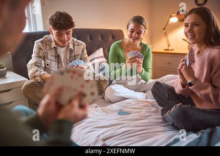 Un gruppo di adolescenti e ragazzi a casa che si divertono ridendo e giocano a carte in camera da letto insieme Foto Stock