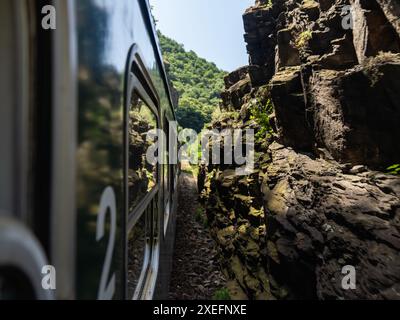 Treno verde che viaggia su binari attraverso uno stretto passaggio tra grandi rocce Foto Stock