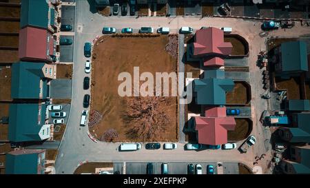 Vista aerea di un quartiere residenziale con case, auto parcheggiate e un'area erbosa centrale con un albero. Foto Stock