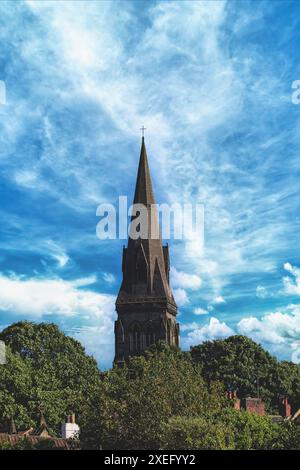 Un alto campanile di chiesa sorge sopra gli alberi circostanti sotto un cielo spettacolare e nuvoloso. Foto Stock