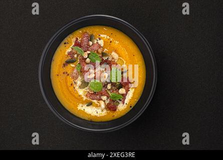 Zuppa di crema di zucca con semi di zucca e pancetta croccante su sfondo nero con spazio per copiare, vista dall'alto Foto Stock