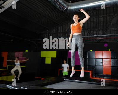 Donna di mezza età felice che pratica e salta sui trampolini in un centro sportivo al coperto, allenamento e moderno concetto di intrattenimento Foto Stock