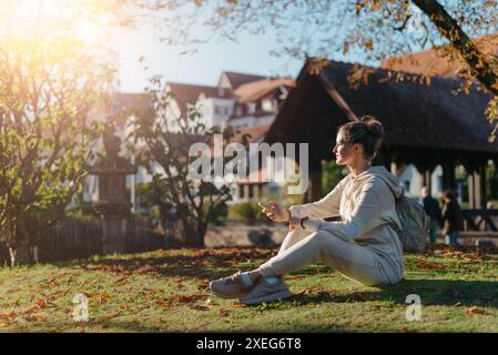 Giovane ragazza adolescente alla moda con smartphone nel Parco Europian in autunno seduta a sorridere. Giovane donna alla moda in autunno a Park Foto Stock