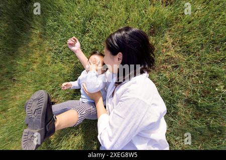 Mamma sorridente asiatica e dolce figlia sono sdraiati su un prato verde Foto Stock