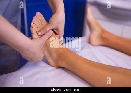 Primo piano del piede femminile con un massaggio delicato. La massaggiatrice tiene la gamba della donna nelle sue mani. Un giovane cliente mente e ama rilassarsi con un professionista Foto Stock